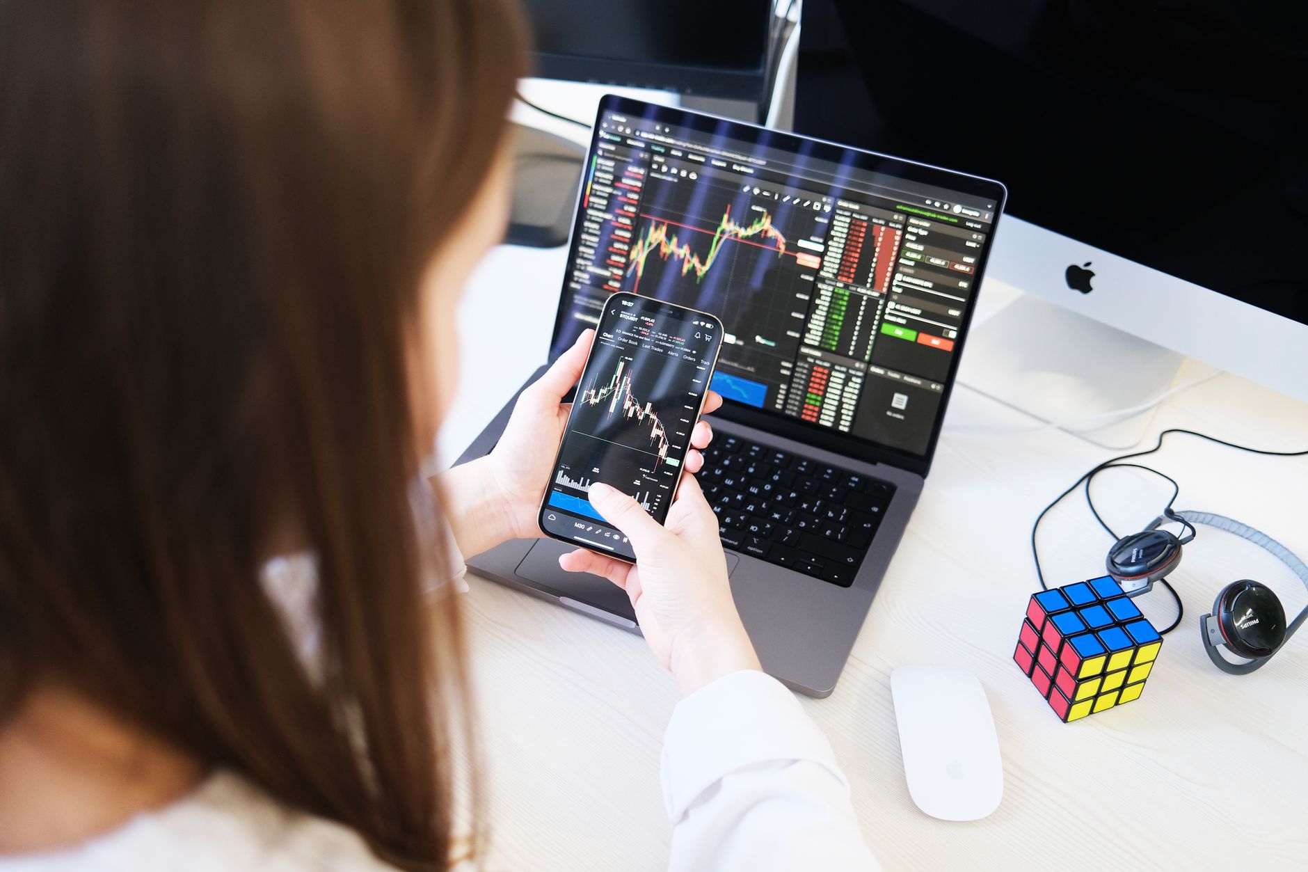 Mulher analisando gráficos financeiros e diagramas de rede em tempo real no laptop e smartphone